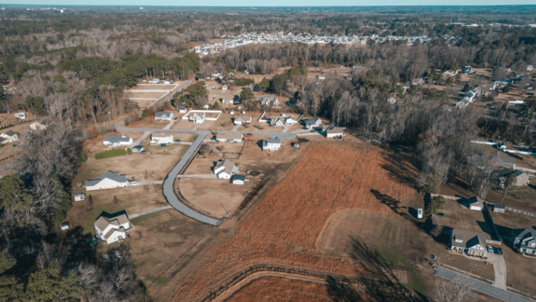 An aerial view of a suburban neighborhood mixed in with farmland and undeveloped, vacant lots.